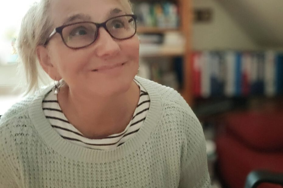 Blonde Frau mit roter Brille und hellem Pullover